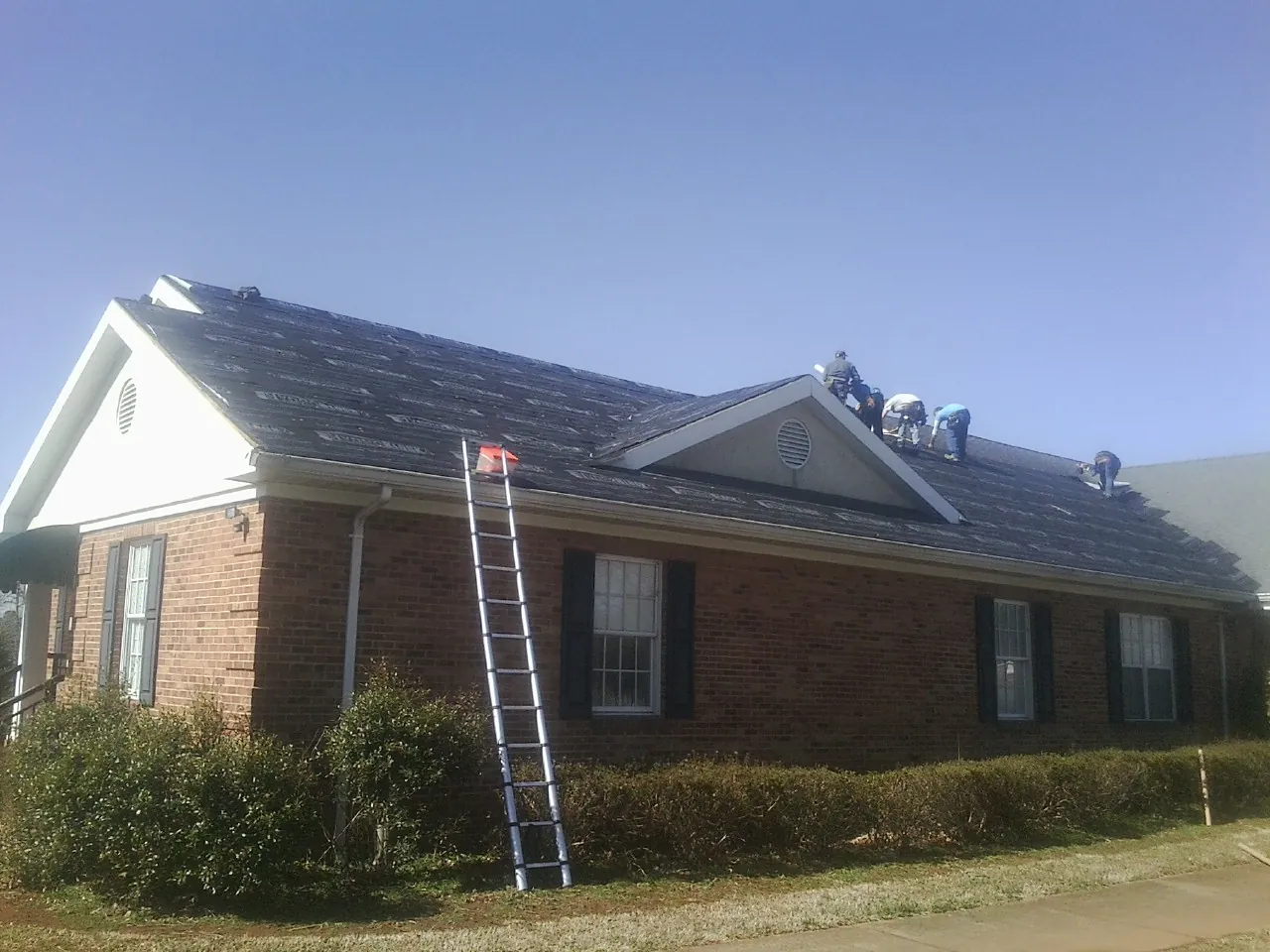 Crew tearing shingles off a brick ranch roof with a ladder set — Emergency Roof Repair work by our crew in Douglas City
