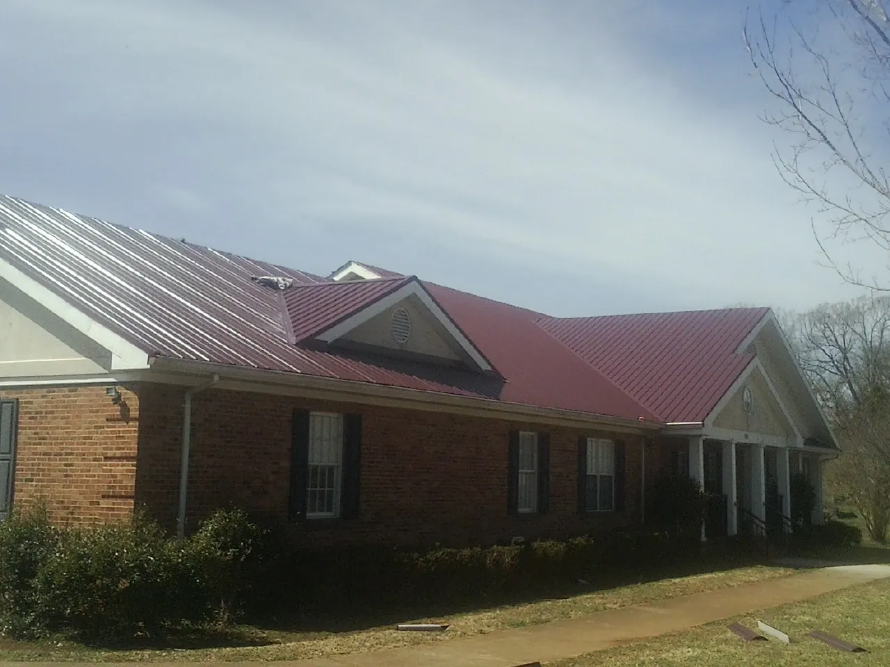 Red metal roof with gabled entries on a long brick building, from a Hail Damage Roof Repair job in Douglas City