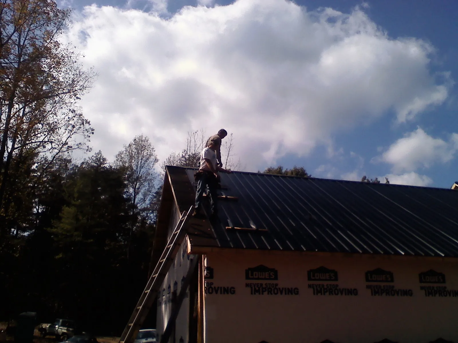 Roofer fastening dark metal panels high against a cloudy sky, from a Roof Inspection job in Douglas City