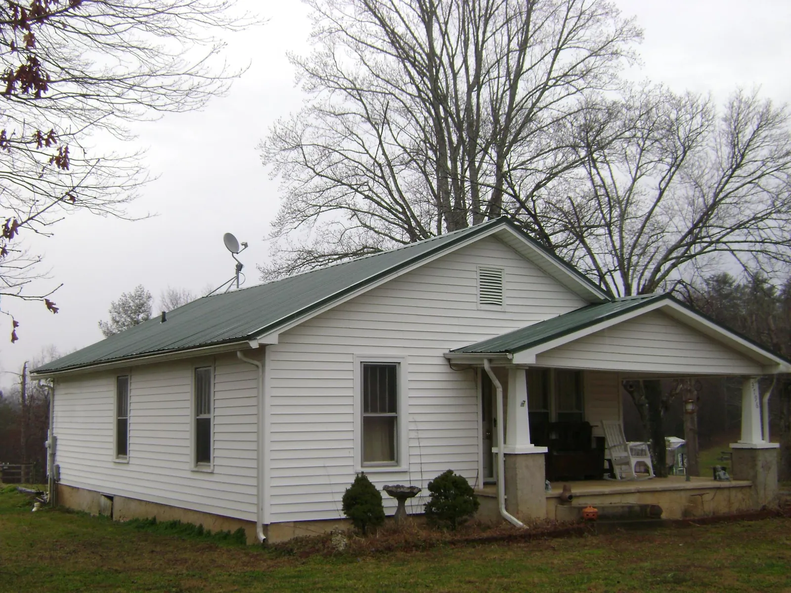 Green metal roof on a white bungalow with a side porch in Douglas City