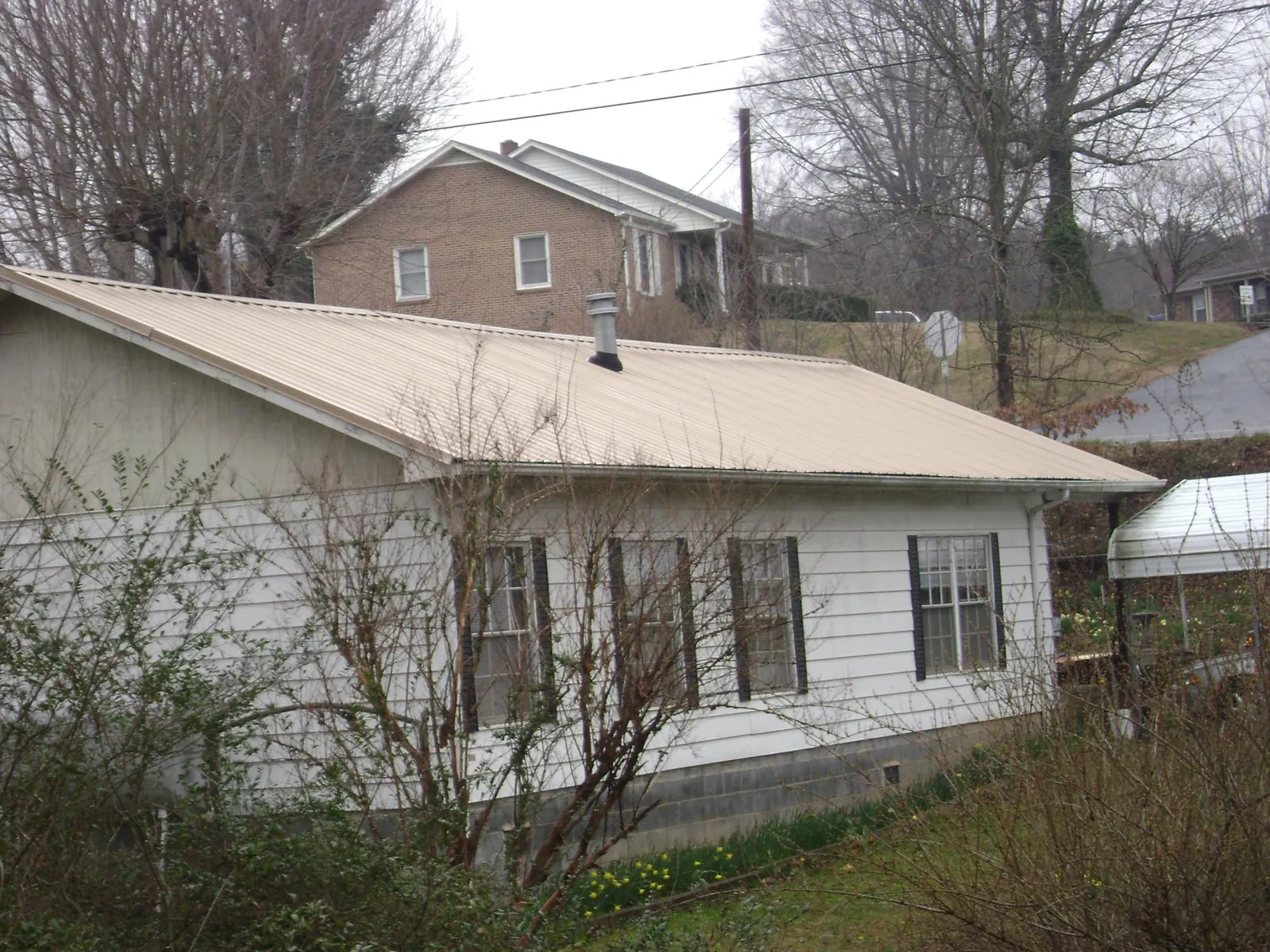 Tan metal roof on a white sided house set into a hillside — Commercial Roofing by Roofing Brothers in Douglas City